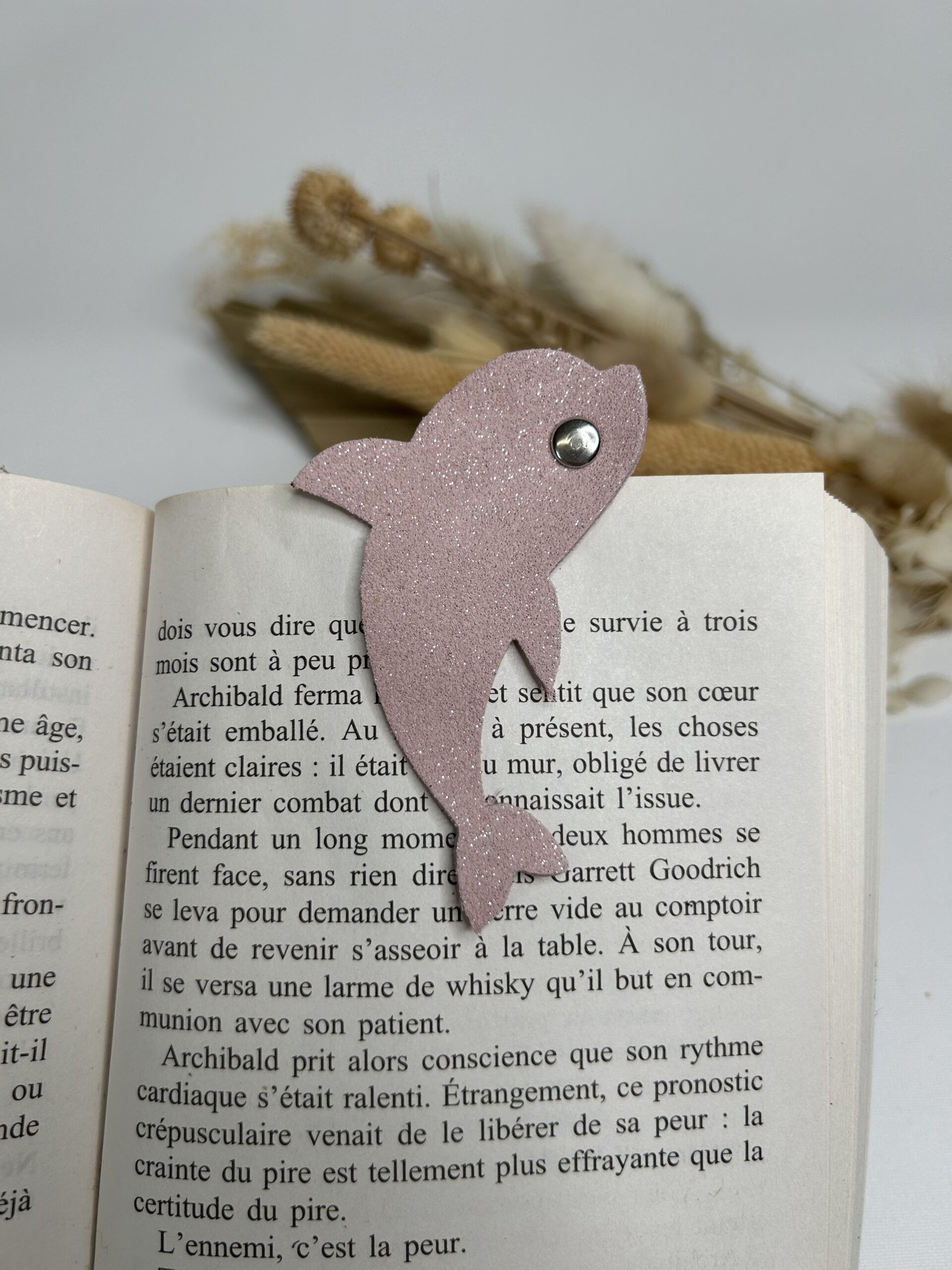Marque-page magnétique en cuir en forme de dauphin fixé sur un livre ouvert, accessoire de lecture artisanal et pratique
