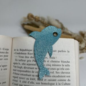 Marque-page magnétique en cuir en forme de dauphin fixé sur un livre ouvert, accessoire de lecture artisanal et pratique