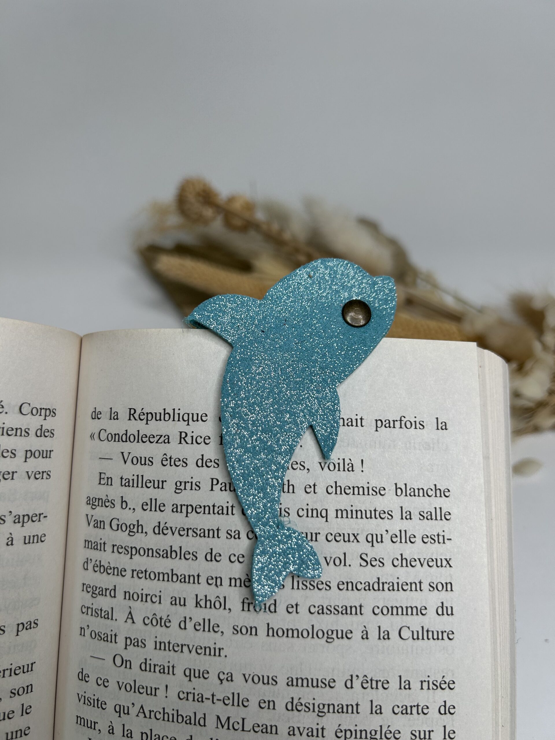 Marque-page magnétique en cuir en forme de dauphin fixé sur un livre ouvert, accessoire de lecture artisanal et pratique