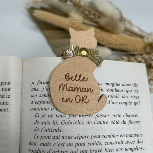 Marque-page magnétique en cuir beige gravé “Belle Maman en OR” en forme élégante posé sur un livre ouvert.