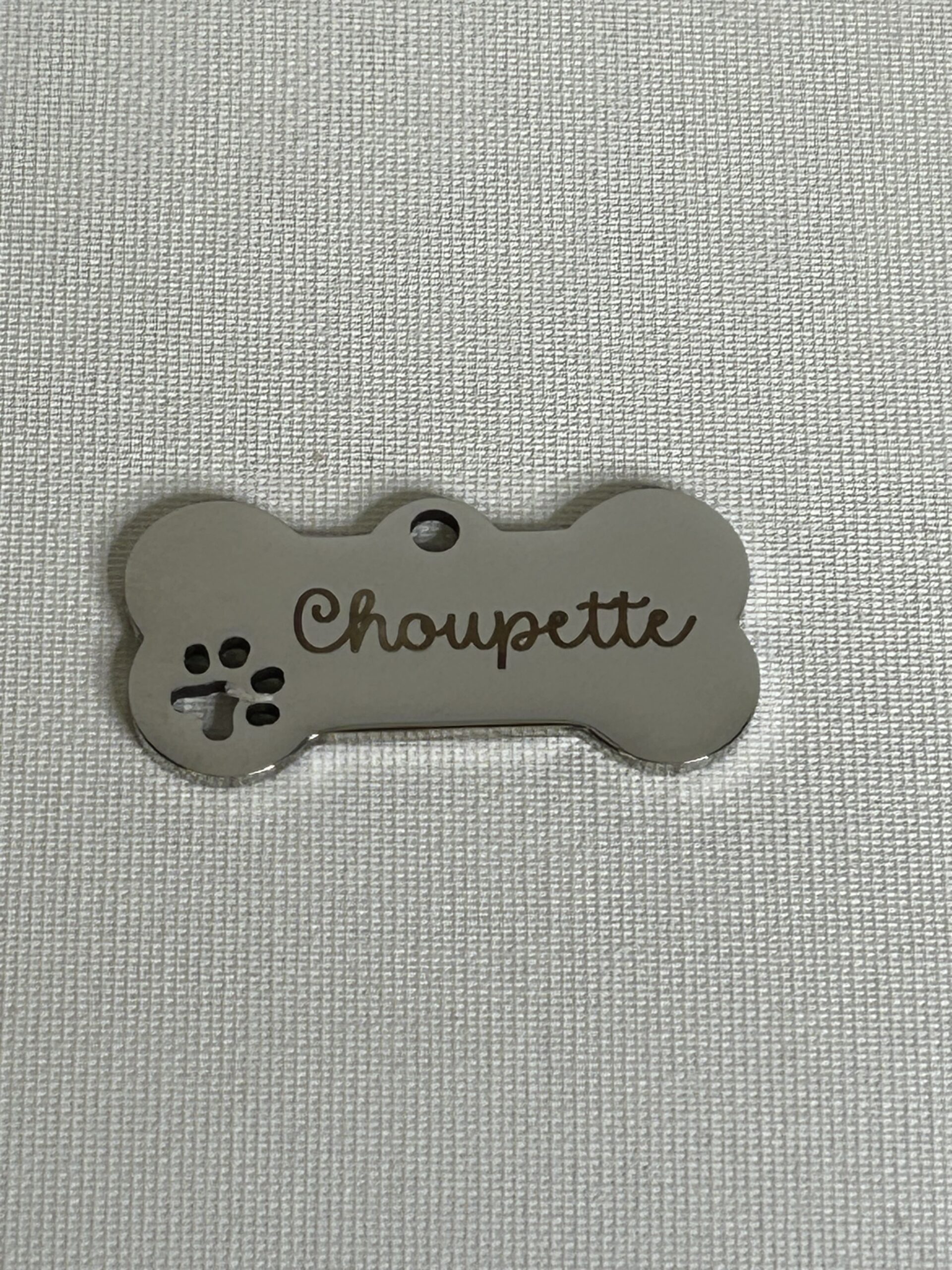 Médaille personnalisée en métal en forme d’os gravée avec le prénom d’un animal et empreinte décorative.