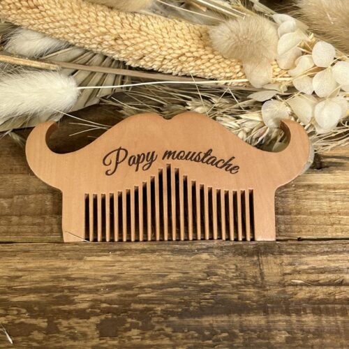 Peigne à moustache et barbe en bois gravé pour papa et papy posé sur fond naturel en bois avec fleurs séchées.