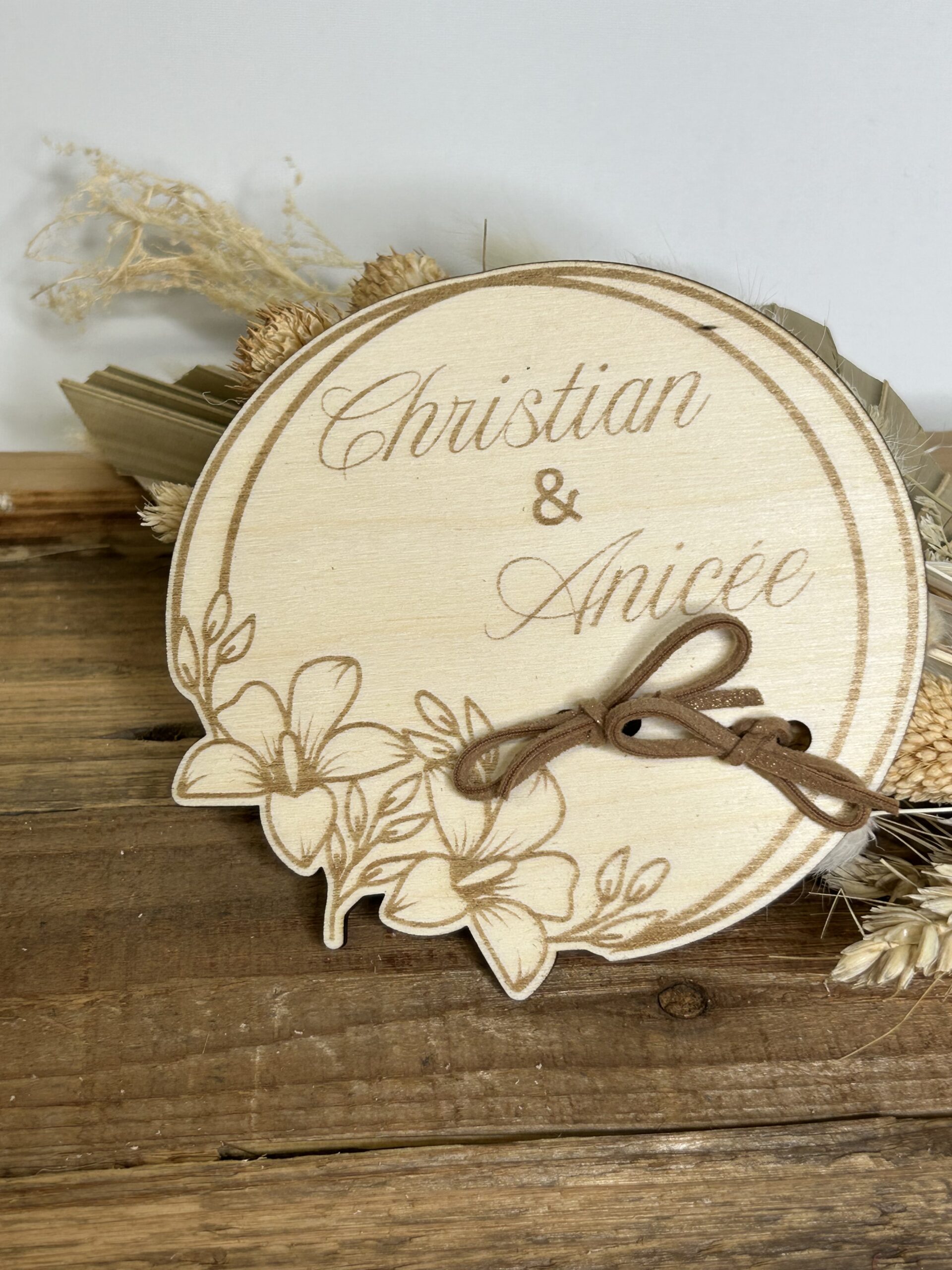 Porte-alliances mariage personnalisé en bois gravé avec prénoms, forme ronde avec décor floral et lien pour maintenir les alliances.